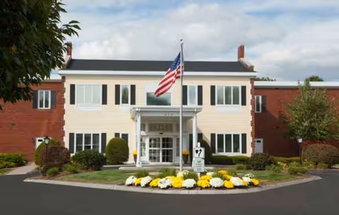 Two-story brick and beige building with flagpole and flower bed at entrance.