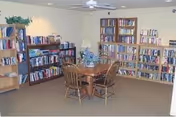 Small community library/reading room with bookshelves along the walls and a round table with four wooden chairs.