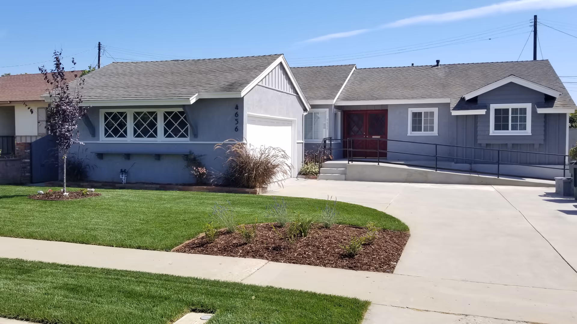 Single-story gray ranch-style house with a manicured front lawn, driveway, and a wheelchair ramp to the front door.