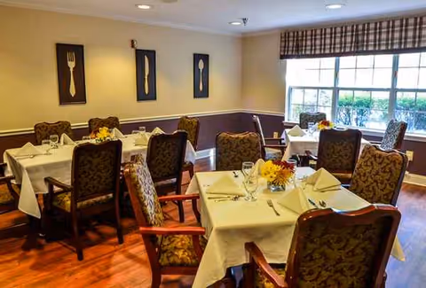 A senior living dining room with tables set for meals and decorative wall art.