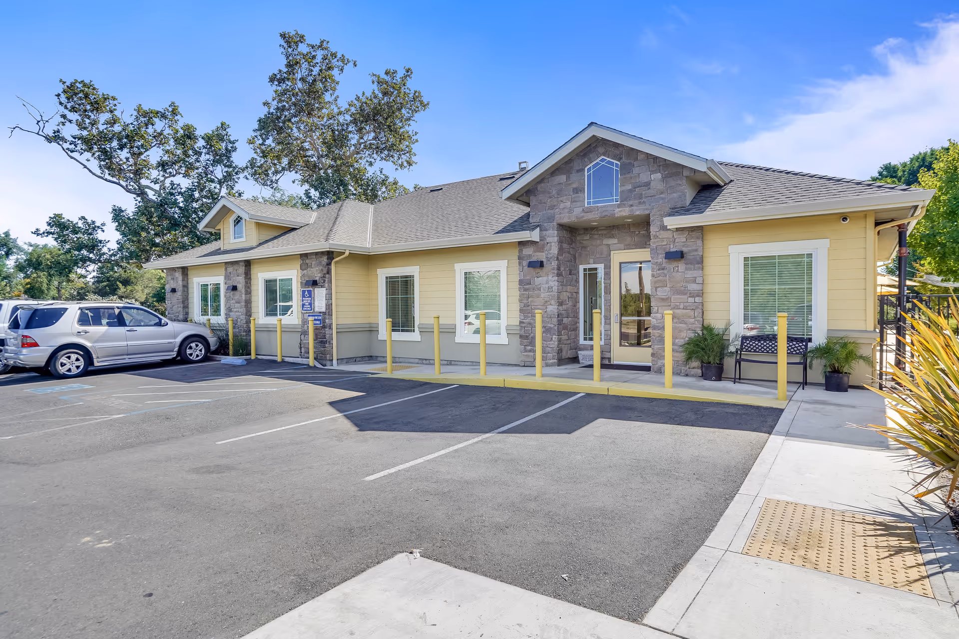 Exterior front of a single-story senior living building with a stone-accented entrance, parking spaces, and landscaping.