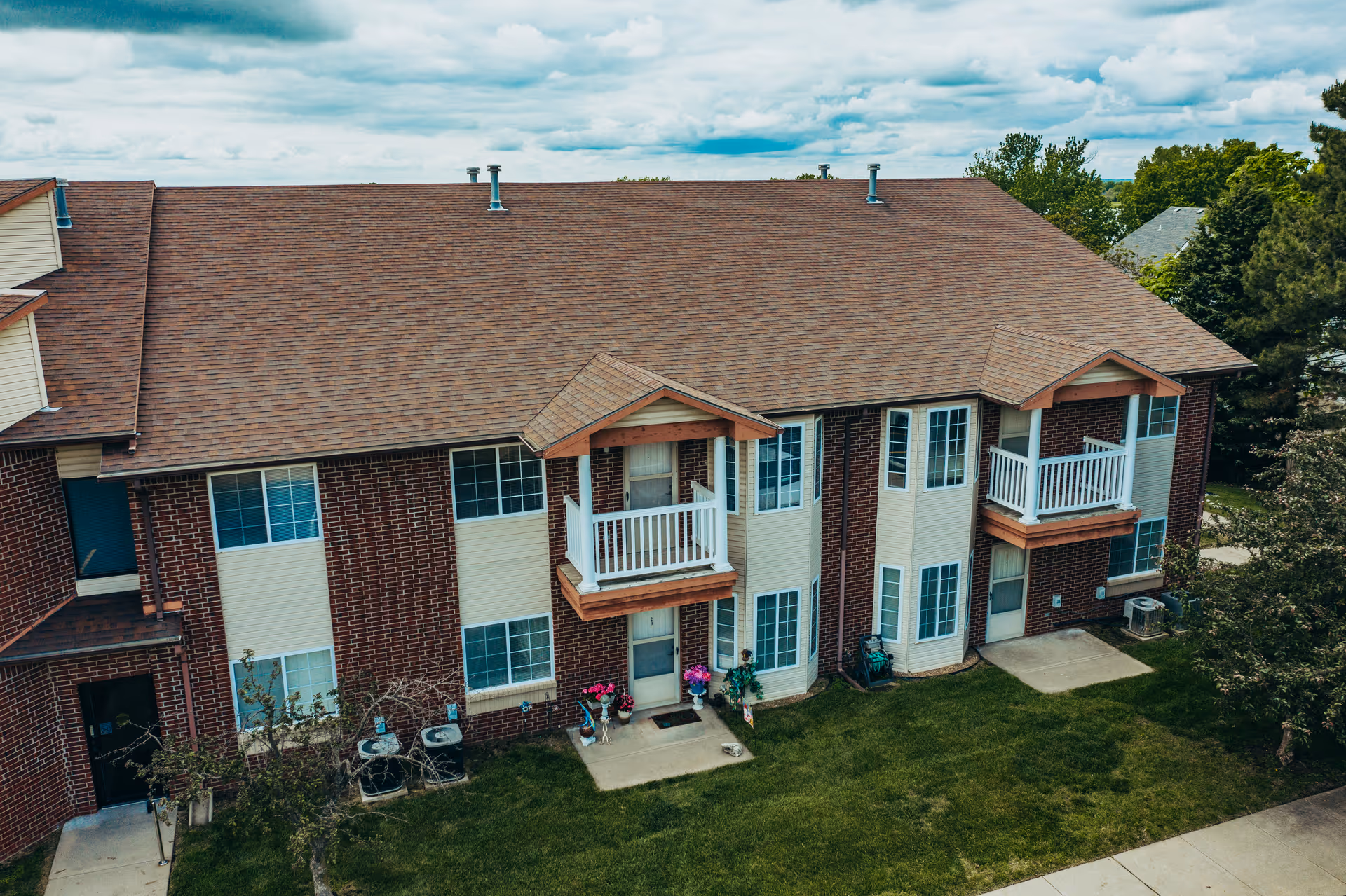 Front exterior of a two-story brick apartment building with small balconies and a grassy lawn.