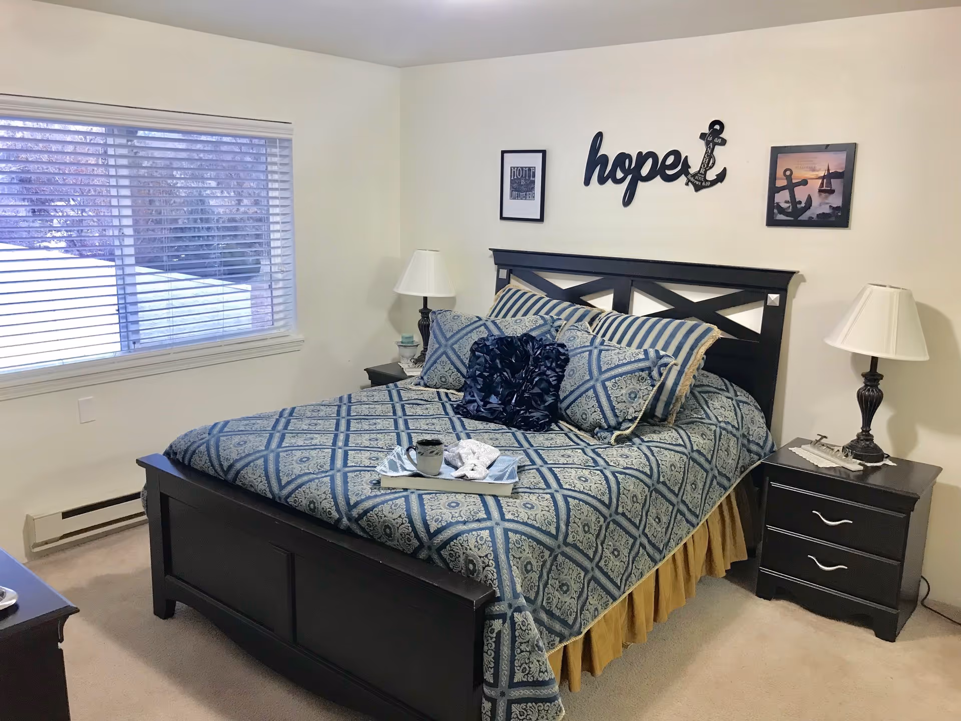 Bright bedroom with a dark wood bed dressed in blue patterned bedding, matching nightstands and lamps, and 'hope' wall decor.