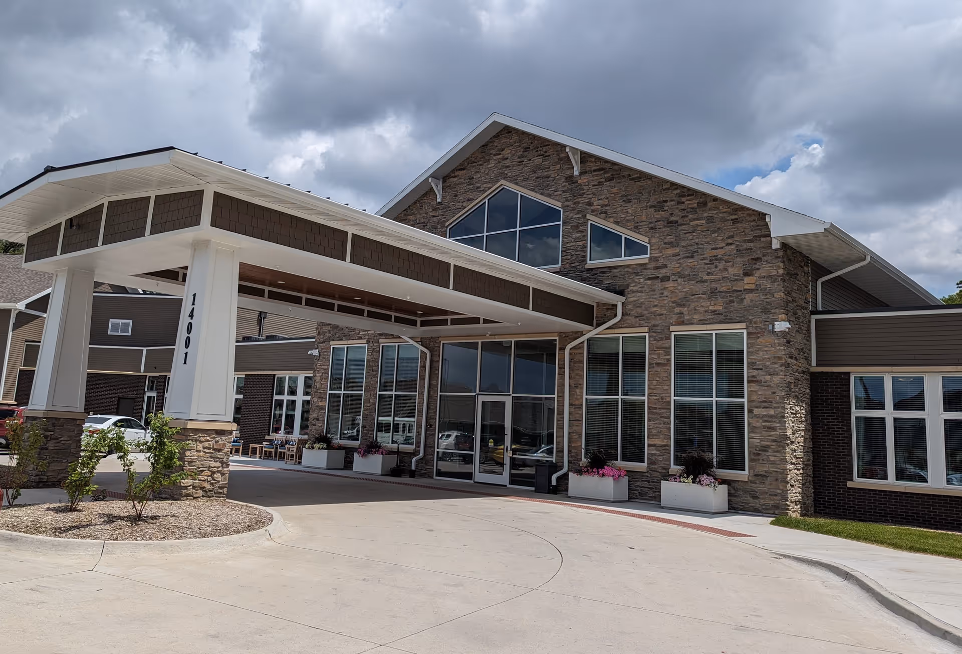 Front entrance of a building with a covered drive-up canopy, stone facade, and large windows.