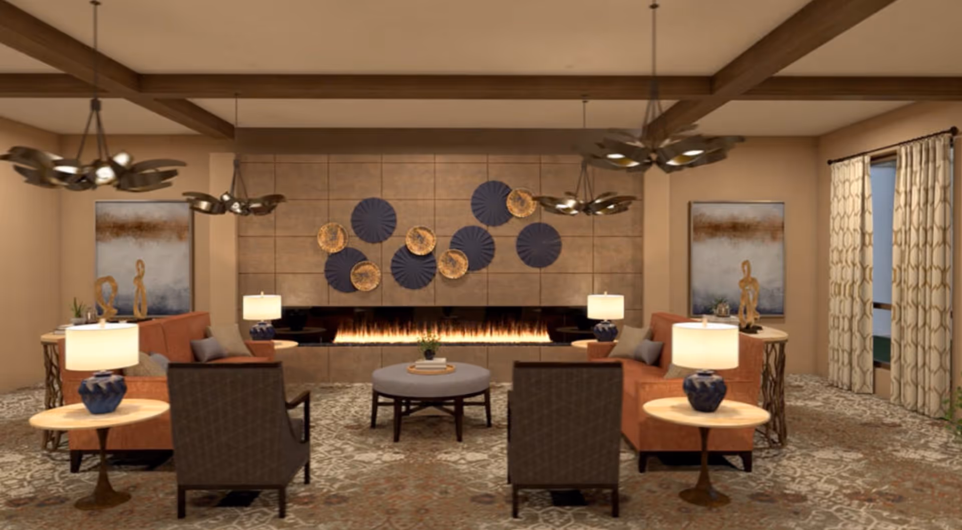 A cozy living room with two orange sofas facing each other, two dark armchairs, a round ottoman in the center, and a modern linear fireplace on the far wall. The wall above the fireplace is decorated with circular art pieces in blue and gold. There are two side tables with blue lamps on either side of the sofas, abstract sculptures on small tables behind the sofas, patterned carpet, and large windows with patterned curtains on the right side. The ceiling has wooden beams and three modern pendant lights.