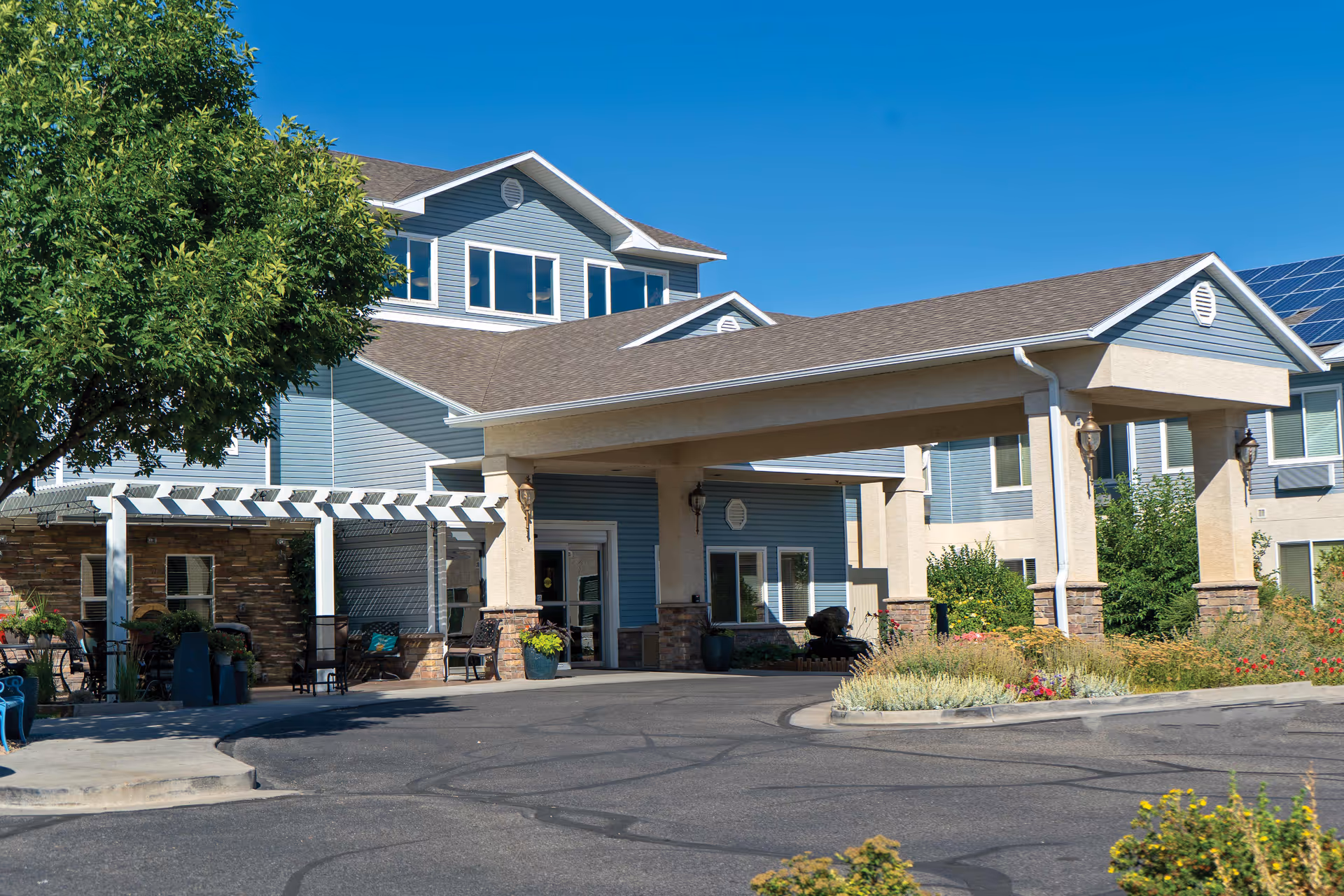 Exterior view of a blue senior living facility with a covered entrance and landscaped driveway