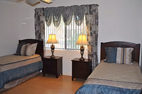 Two twin beds with matching bedding, nightstands and lamps arranged beneath a window with curtains.
