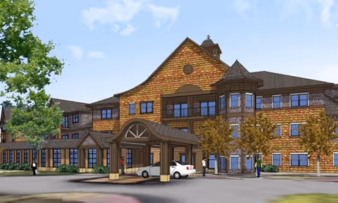 Exterior view of a large multi-story senior living facility with a covered entrance, several windows, trees, and a few people walking near the building under a partly cloudy sky.
