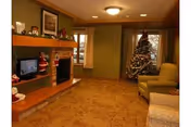 Cozy living room decorated for Christmas with a fireplace, a Christmas tree, a television, and comfortable seating including armchairs and a sofa.