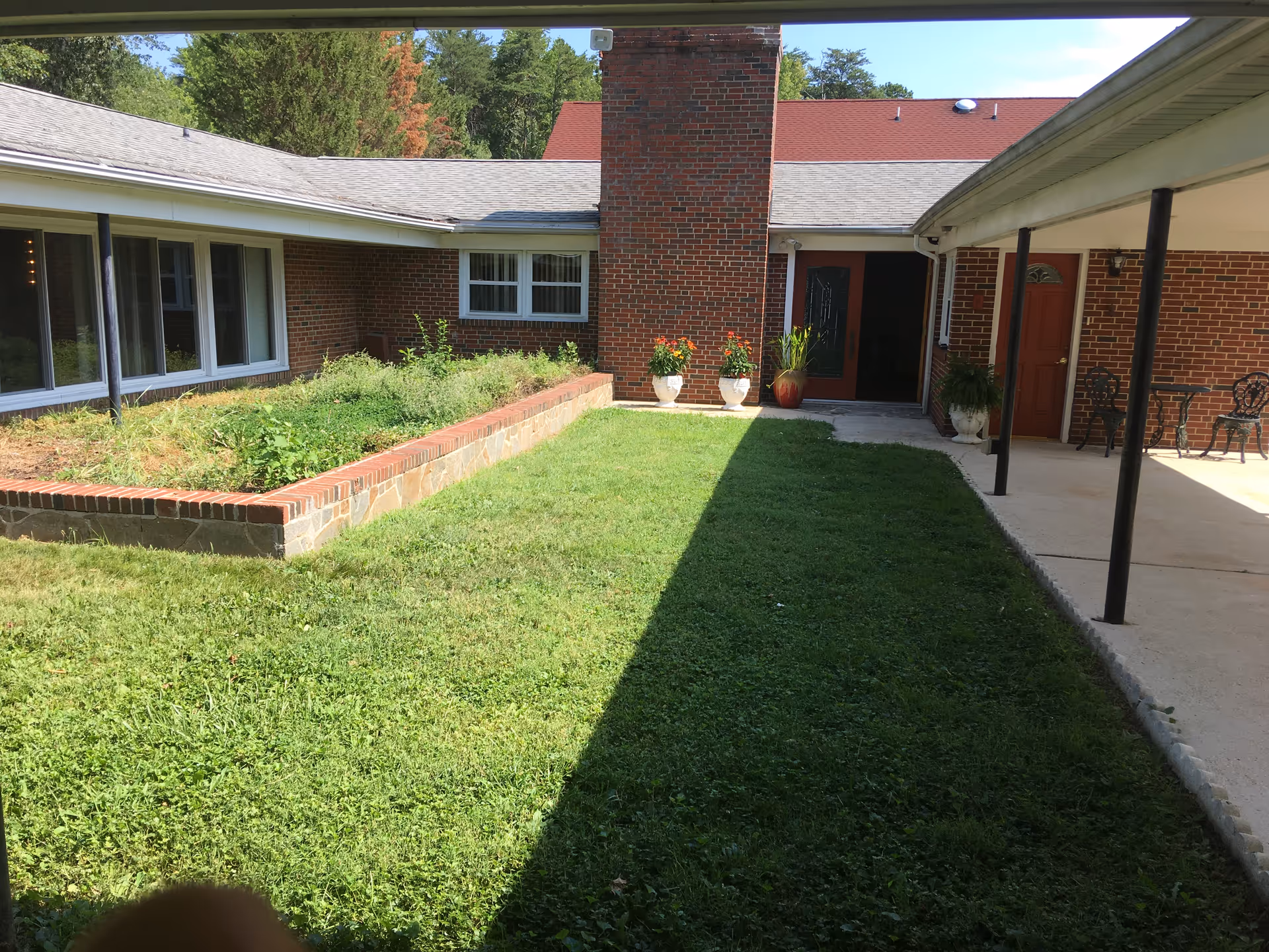 Grassy interior courtyard with a raised brick planter, potted plants, and a covered walkway between brick building wings.