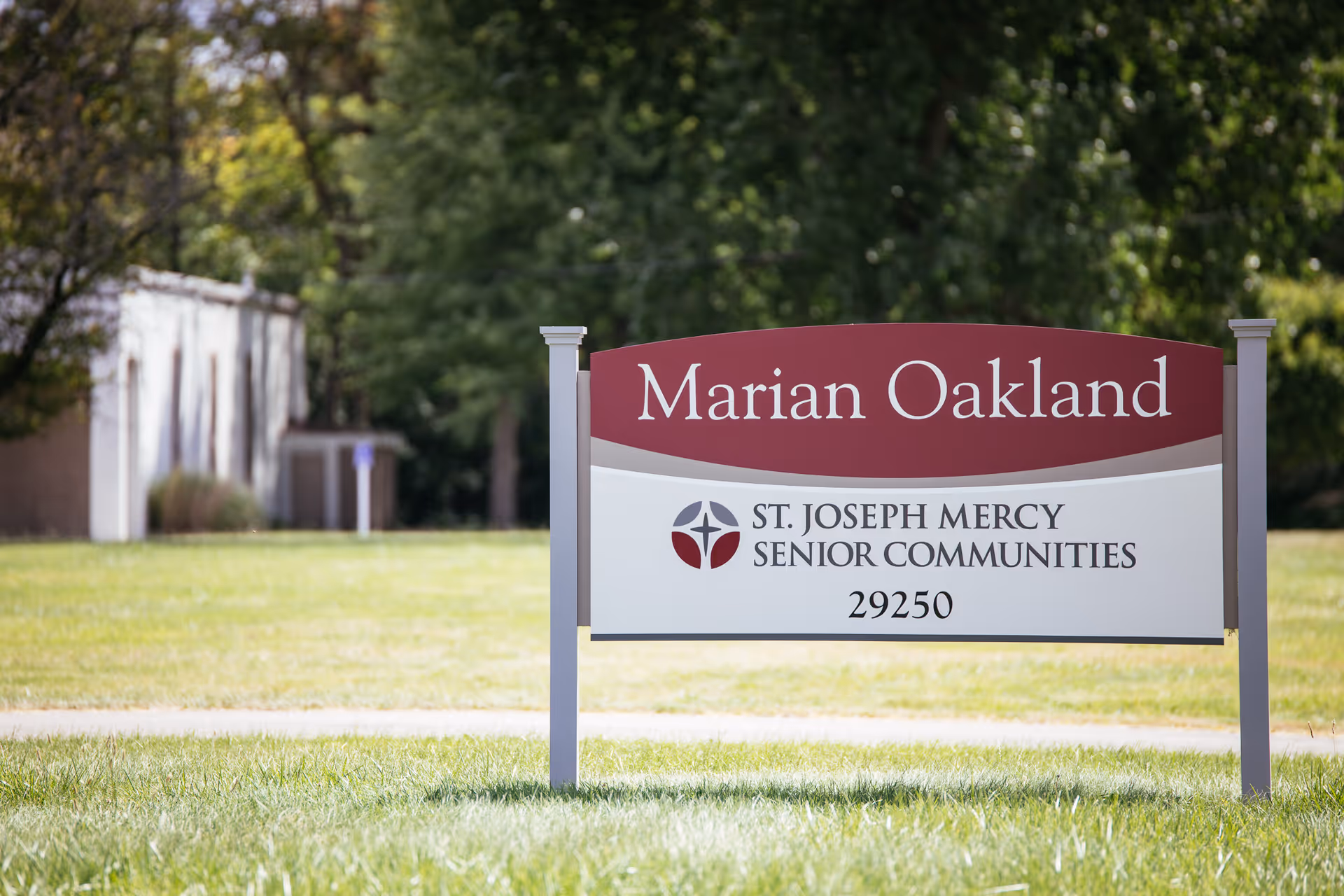 Outdoor sign for Marian Oakland, part of St. Joseph Mercy Senior Communities, standing on a grassy area with trees and a building in the background.