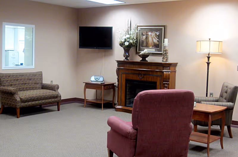 A cozy seating area with upholstered chairs and a loveseat facing a decorative fireplace, wall-mounted TV, and floor lamp.