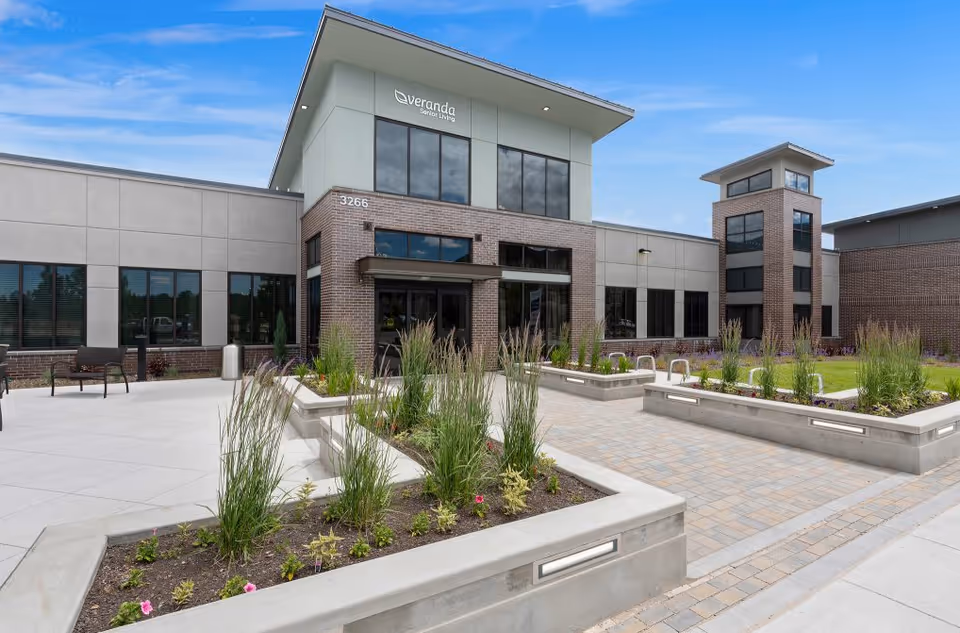 Exterior view of a modern senior living facility with glass entrance and landscaped planters.