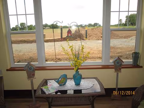 Indoor sitting area with wicker table, yellow vase, birdhouse decorations, and large window view.