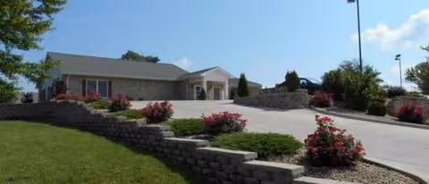 Exterior view of a senior living facility with a sloped driveway and landscaped front yard.