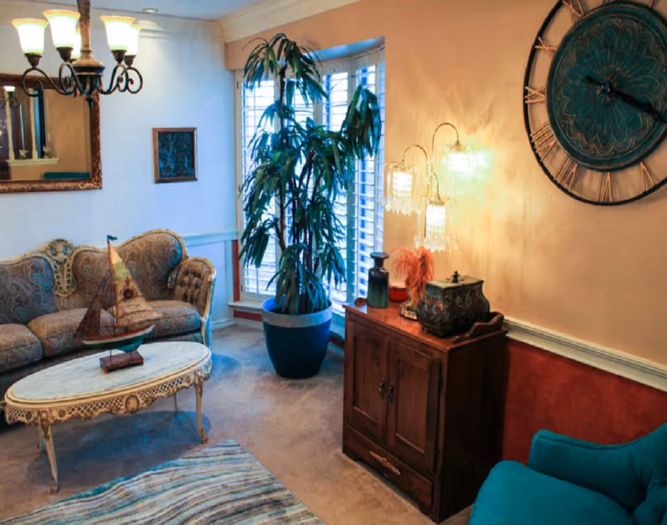 Cozy living room with an upholstered sofa, ornate coffee table, large potted plant, wooden cabinet and wall clock.