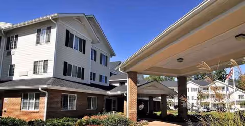 Two-story white senior living building with brick entrance and landscaped front yard.