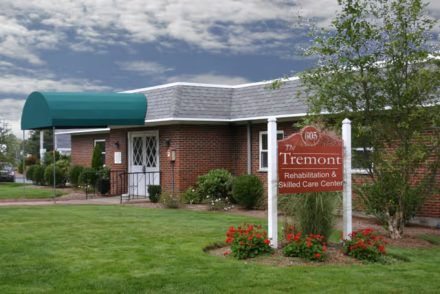 Brick single-story building with a green awning and a front sign for The Tremont Rehabilitation & Skilled Care Center on a manicured lawn.