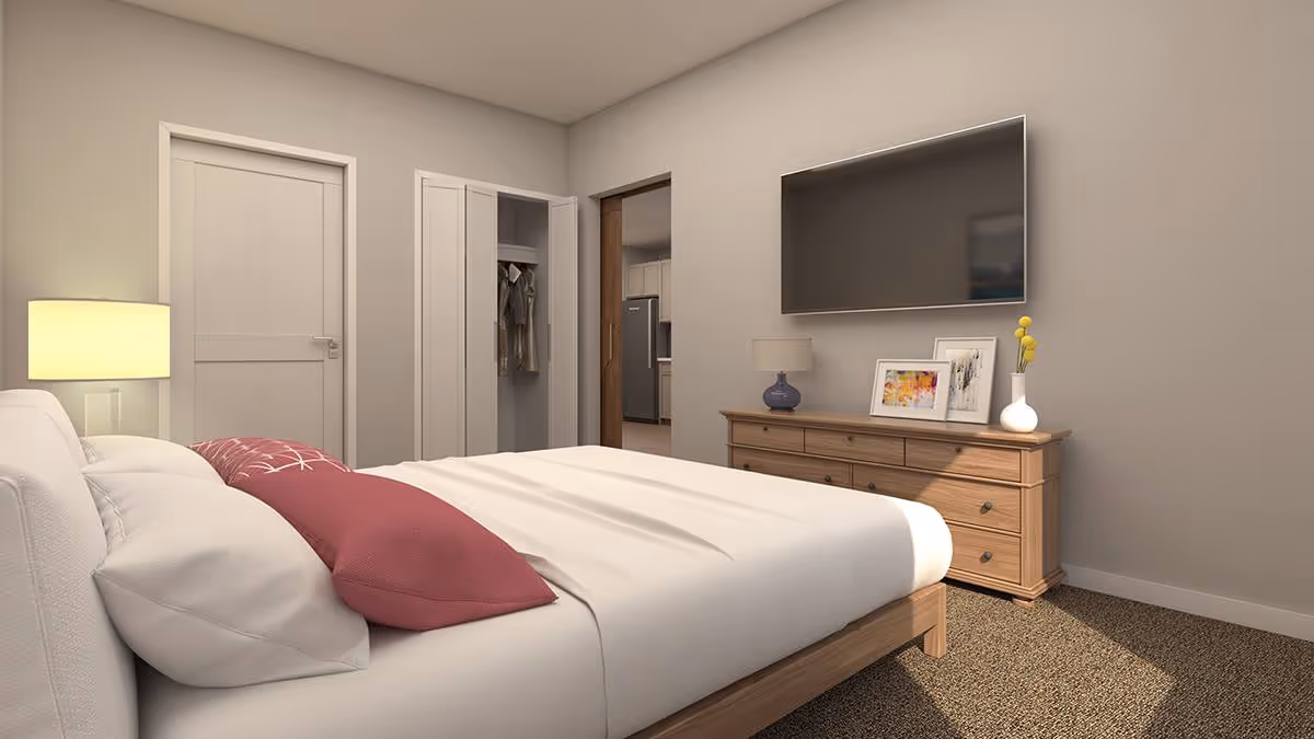 A bedroom with a neatly made bed featuring white sheets and a red pillow. There is a wooden dresser with a lamp, framed pictures, and a vase with yellow flowers. A large flat-screen TV is mounted on the wall above the dresser. The room has a closet with open doors showing hanging clothes, a closed door, and an open doorway leading to a kitchen area.