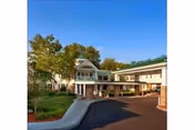 Exterior view of Hanover Hill Health Care Center showing a two-story building with a covered entrance driveway, surrounded by trees and landscaping under a clear blue sky.