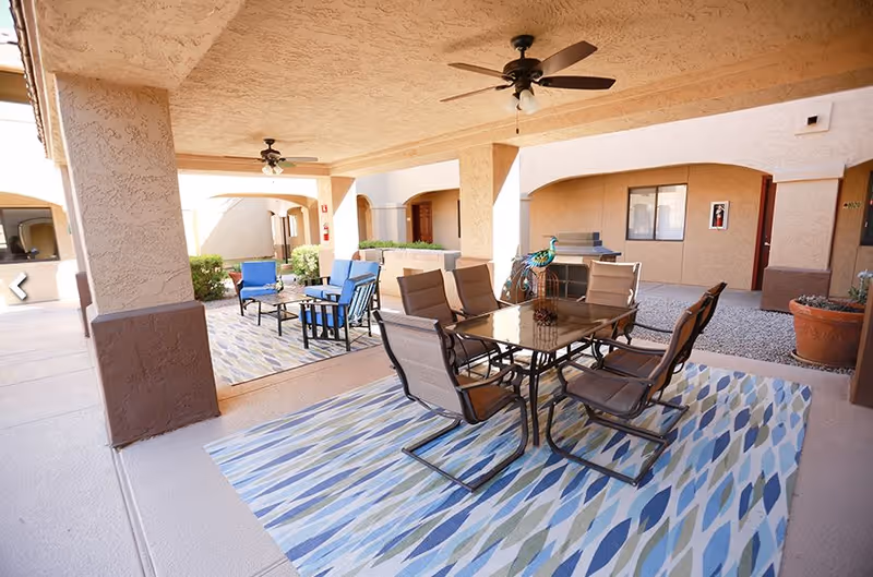 Covered courtyard patio with a glass-top dining table and six chairs, additional lounge seating, ceiling fans, and patterned outdoor rugs.