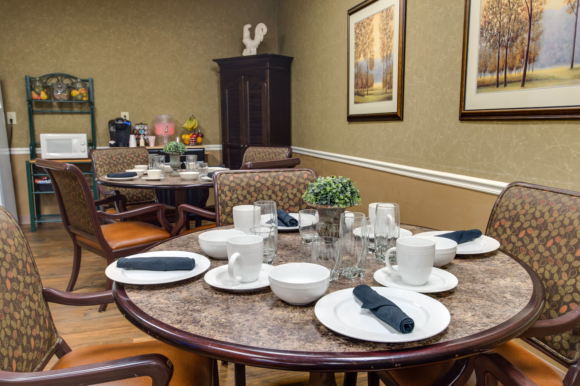 Round dining tables set with white plates, cups, glassware, and dark napkins in a decorated dining room.