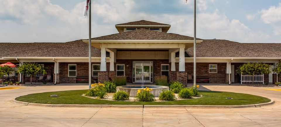 Brick senior living facility front entrance with circular driveway and landscaped fountain.