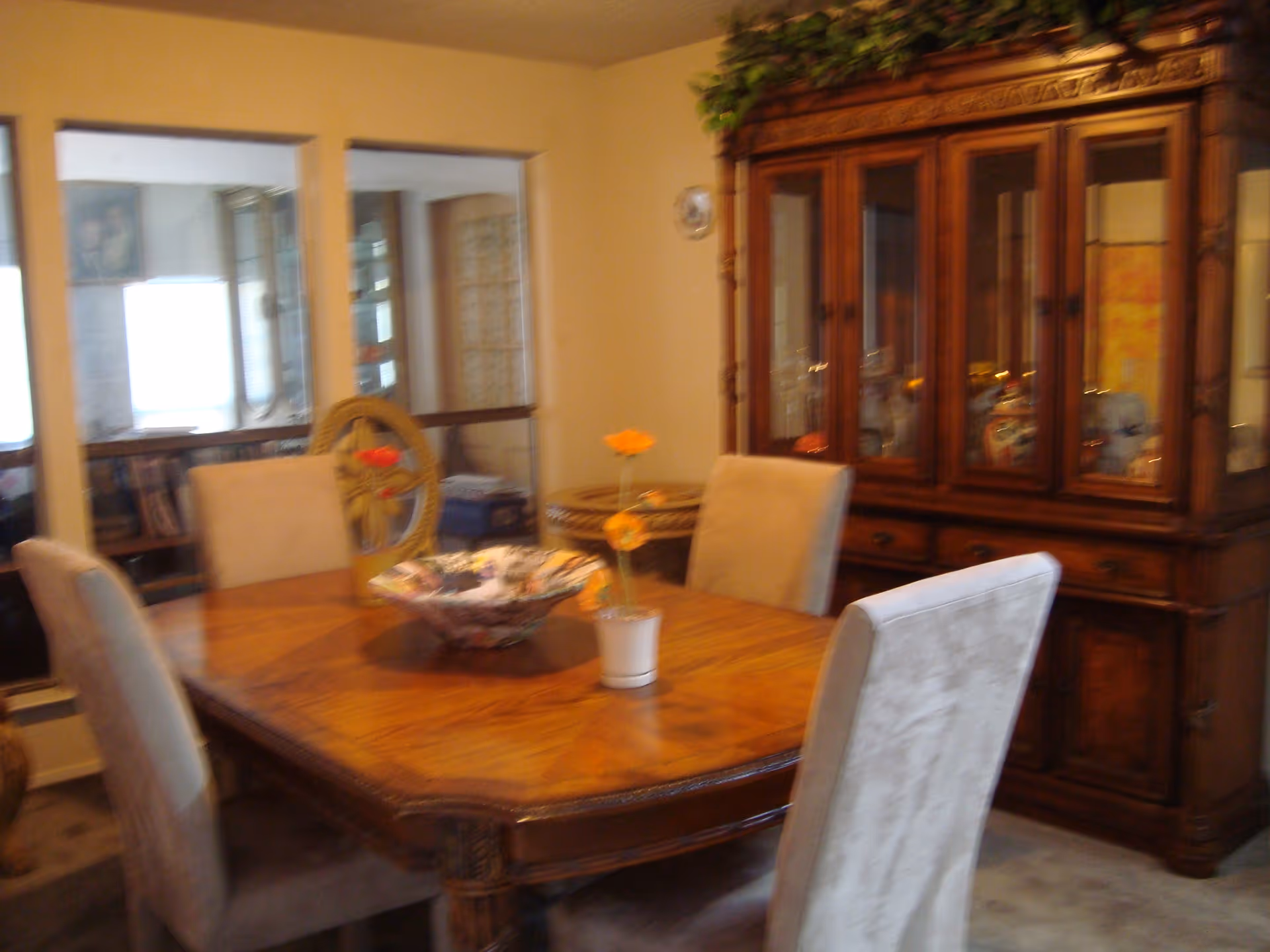 Dining room with a wooden table, upholstered chairs, a floral centerpiece, and a large china cabinet.