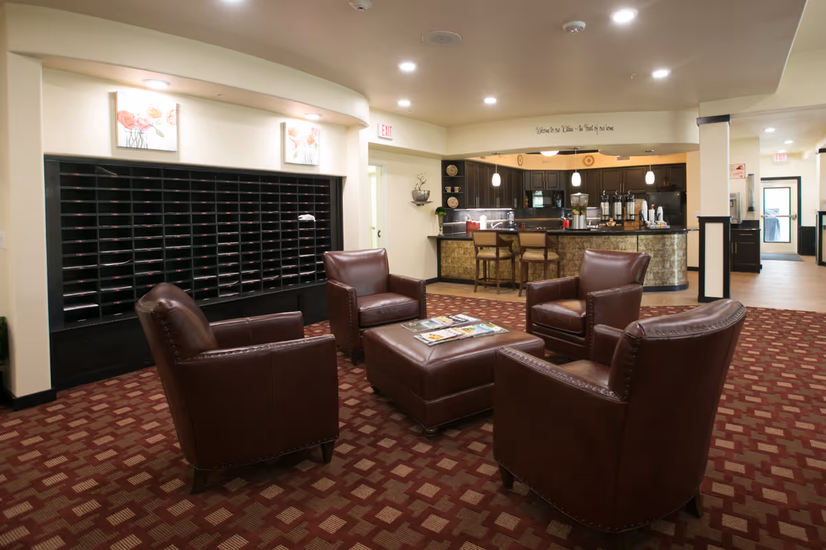 A lounge-style common area with four leather chairs around an ottoman, a mail cubby wall on the left, and a kitchenette/coffee bar in the background.
