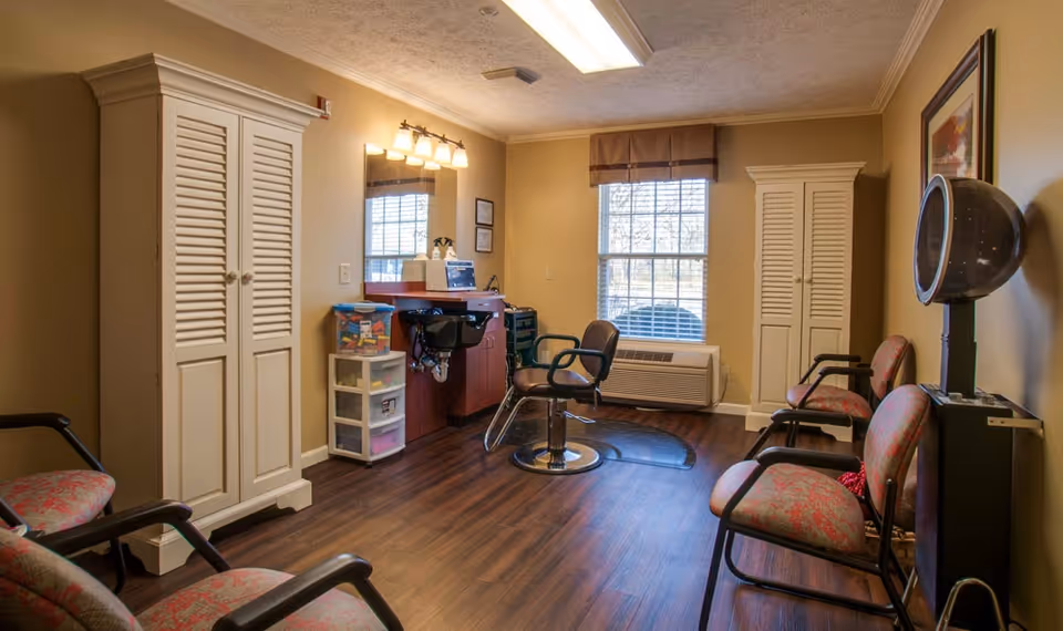 Interior salon room with a styling chair and sink, multiple waiting chairs, a hooded hair dryer, and storage cabinets.