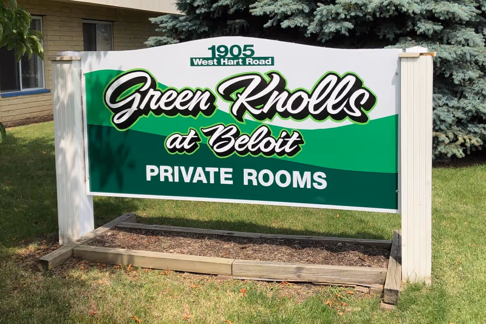 Outdoor sign reading 'Green Knolls at Beloit — Private Rooms' mounted on posts in front of a building and lawn.