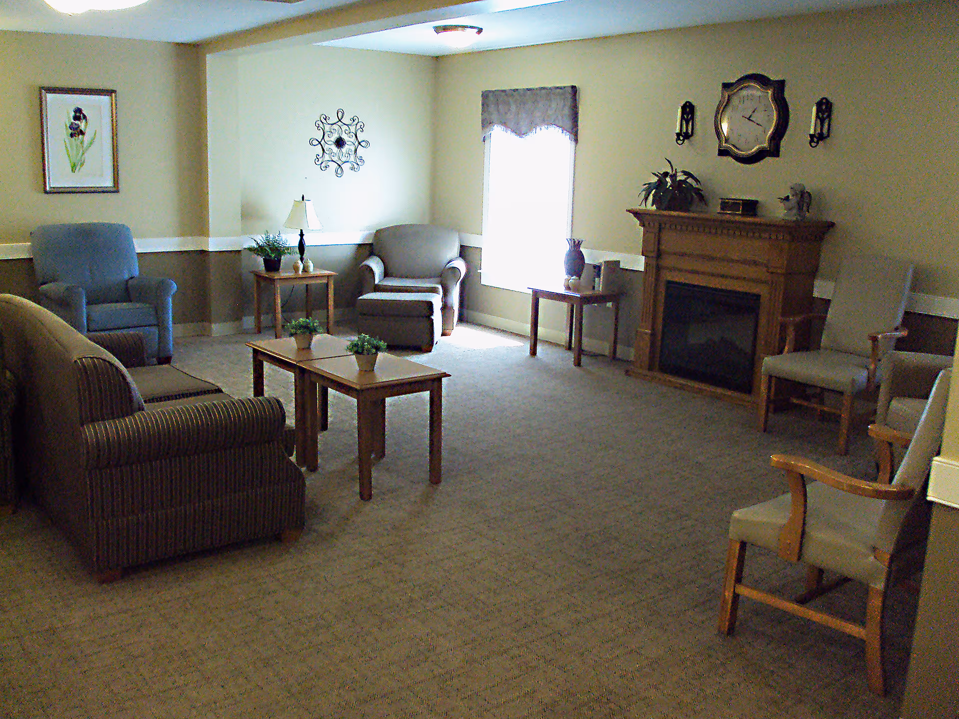 A comfortable senior living lounge with sofas, armchairs, coffee tables, and a fireplace.