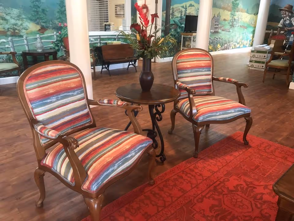 Two striped upholstered armchairs flanking a small round table with a vase of flowers in a decorated common room.