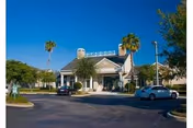 Exterior view of a single-story building with a peaked roof and columns at the entrance, surrounded by palm trees and a parking lot with several cars parked in front under a clear blue sky.