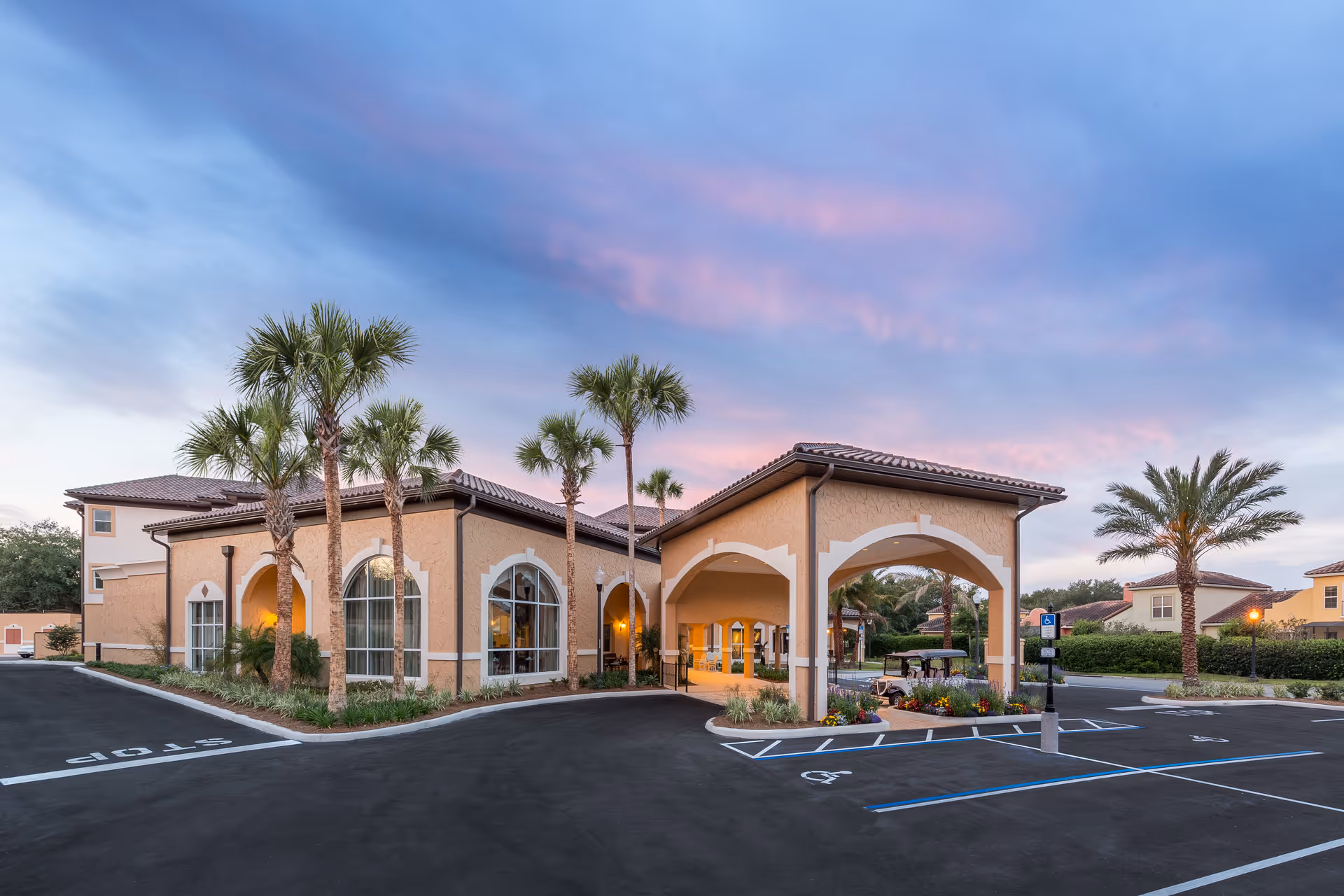 Exterior view of Watercrest Spanish Springs facility at dusk with palm trees, arched entrance, and parking spaces including handicapped spots in front.