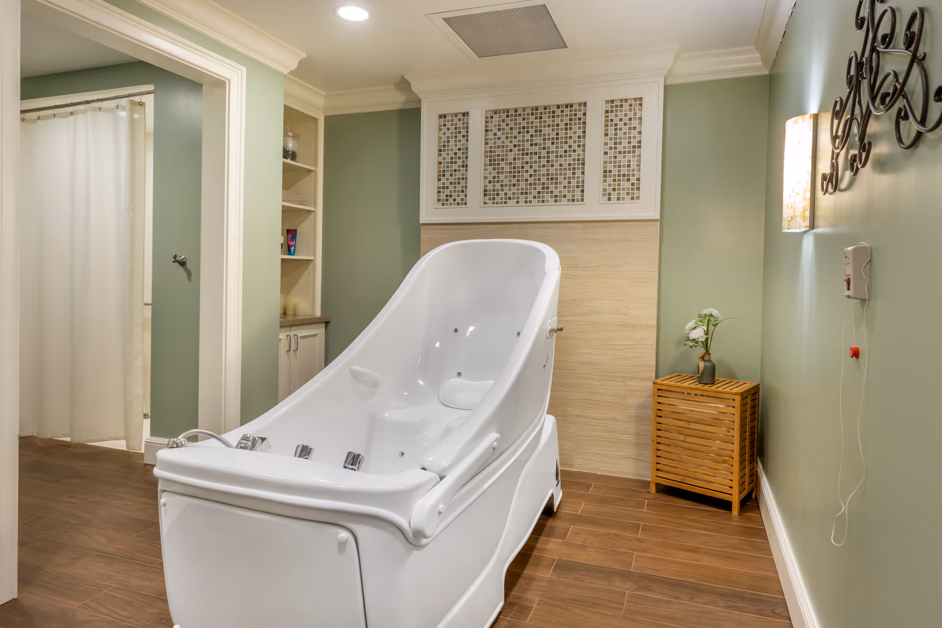 Reclining white therapeutic bathtub in a spa-like bathroom with green walls, wood-look flooring, and a small wooden cabinet.