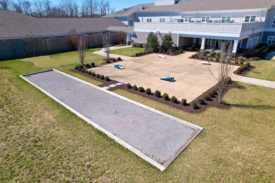 Outdoor recreational area at The Goldton at Spring Hill featuring a bocce ball court and a putting green, surrounded by grass and landscaping, with a two-story building in the background.