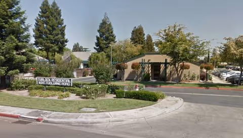Exterior view of Turlock Residential facility with sign, trees, and driveway.