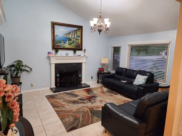 Living room with a fireplace and painting, leather sofas, patterned area rug, chandelier, and large windows.