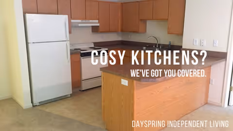 A kitchen with wooden cabinets, a white refrigerator, a white stove with an oven, a range hood, and a countertop with a sink. The kitchen has a light-colored floor and walls. Text on the image reads 'COSY KITCHENS? WE'VE GOT YOU COVERED.' and 'DAYSPRING INDEPENDENT LIVING'.