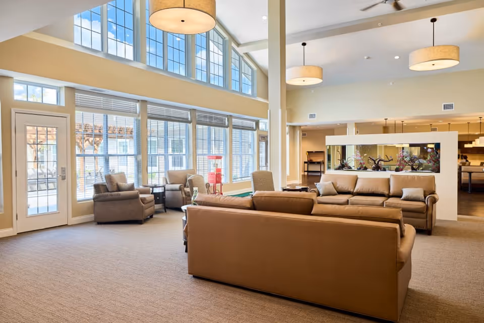 Bright, spacious senior living lounge with leather sofas, armchairs, large windows and pendant lights.