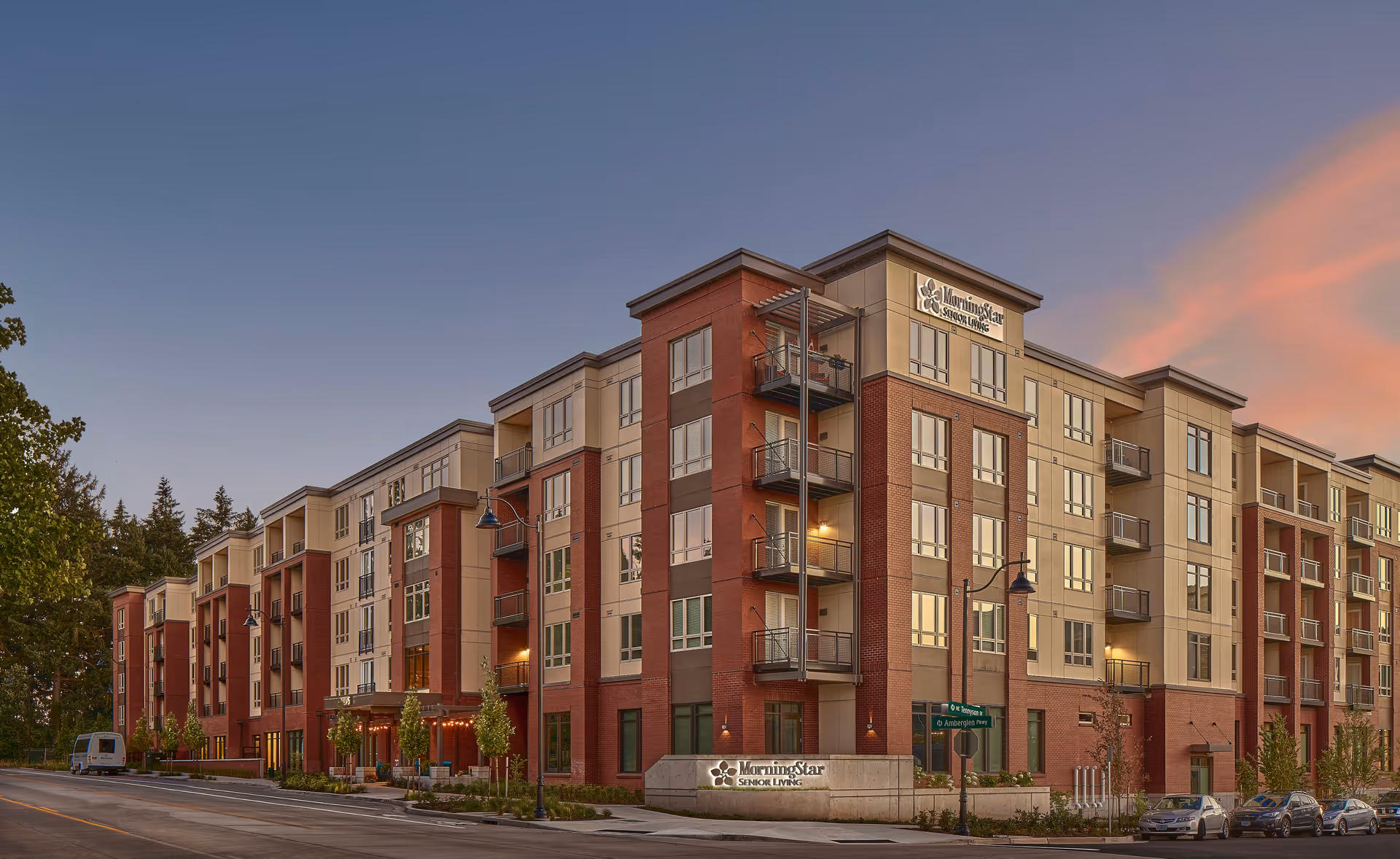 Exterior view of a multi-story senior living facility building named MorningStar Senior Living of Hillsboro during sunset, with a clear sky and street lamps along the sidewalk.