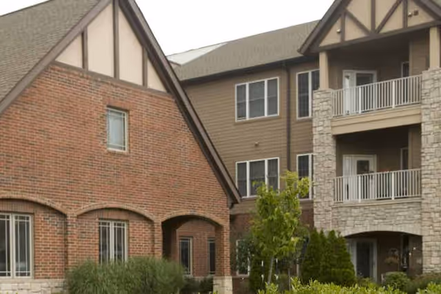 Exterior view of a multi-story senior living building with brick and stone facades, balconies, and landscaped shrubs.