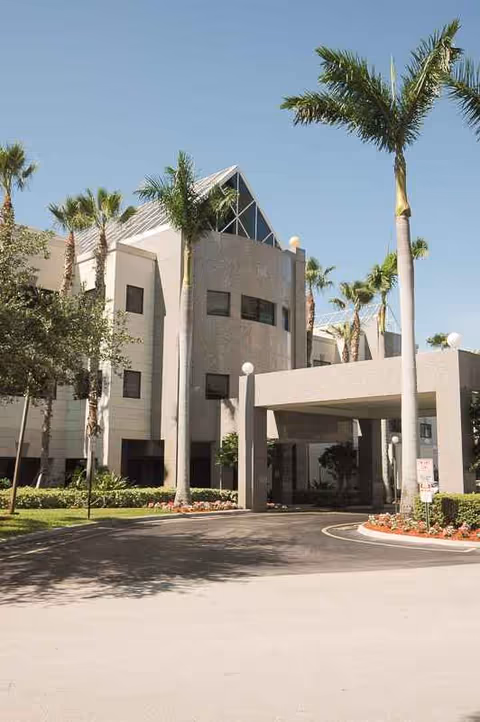 Exterior view of The Gardens Court facility with palm trees and an entrance canopy.