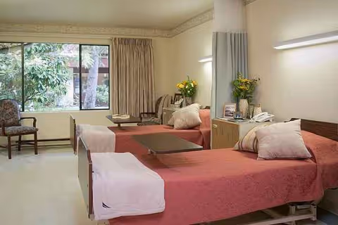 Two pink-covered hospital beds in a bright patient room with a window view.