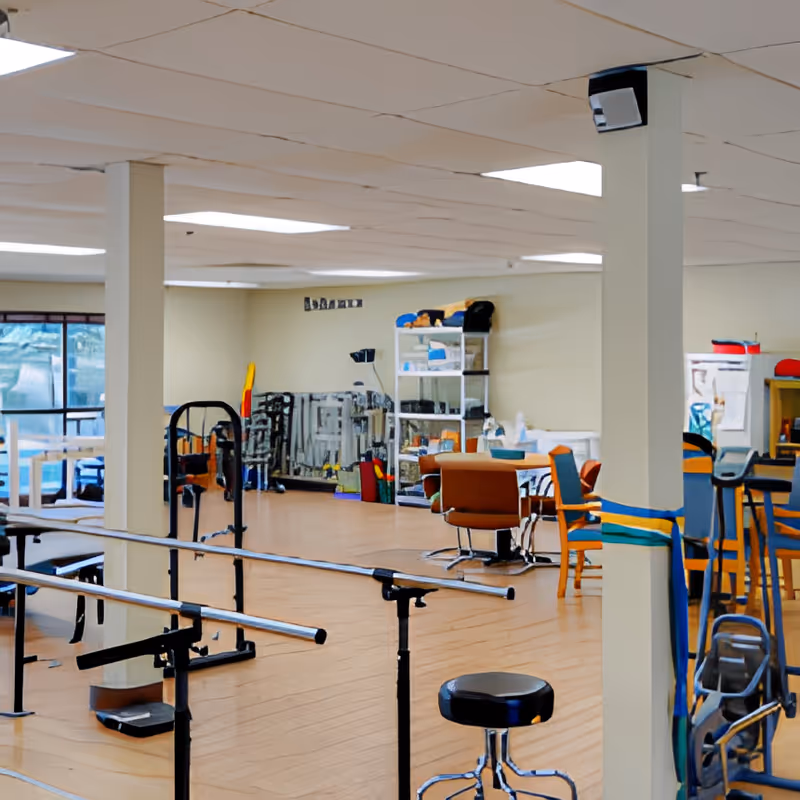 Open therapy gym with parallel bars, exercise equipment, chairs and shelving in a senior living facility.