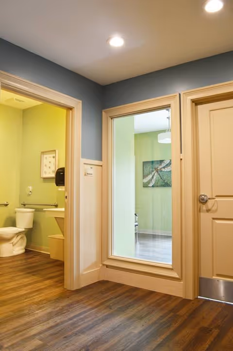 Interior hallway with wood floors showing an open bathroom and a windowed room with green walls.