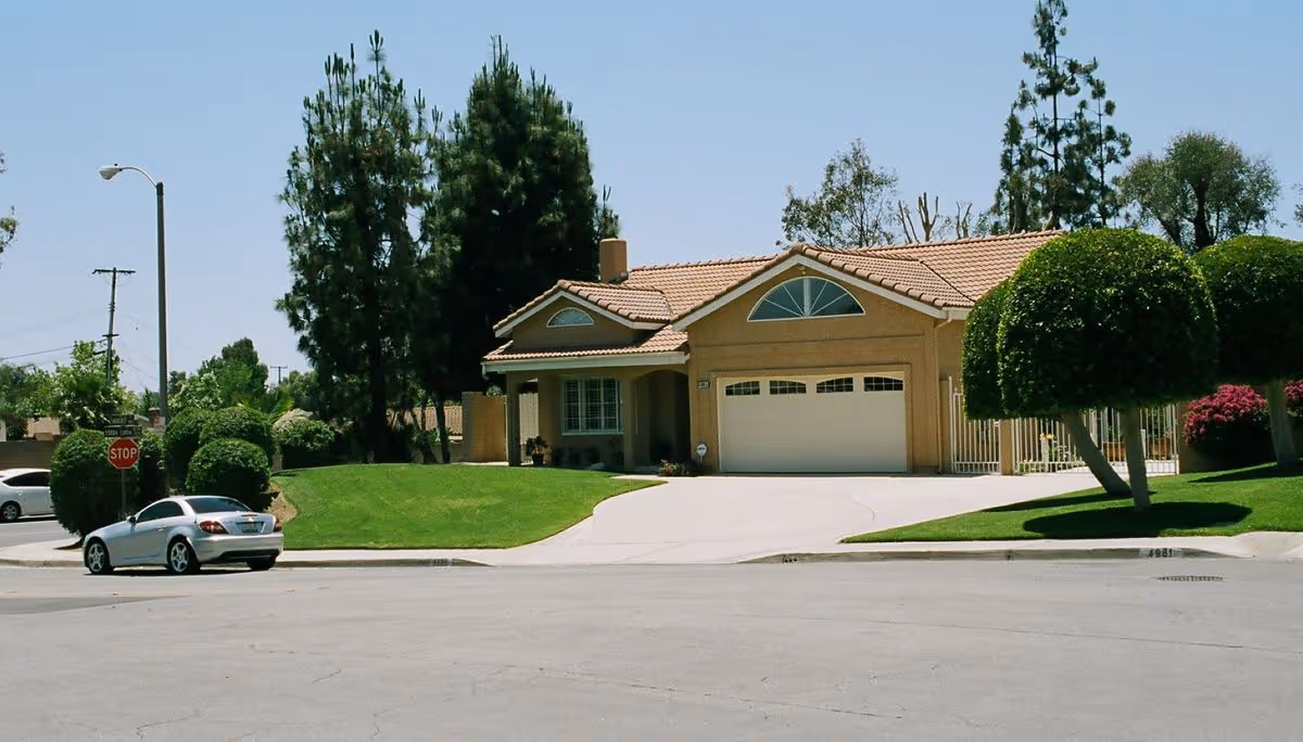 Front view of a single-story suburban house with a tiled roof, two-car garage, curved driveway, manicured lawn, and a parked car at the curb.