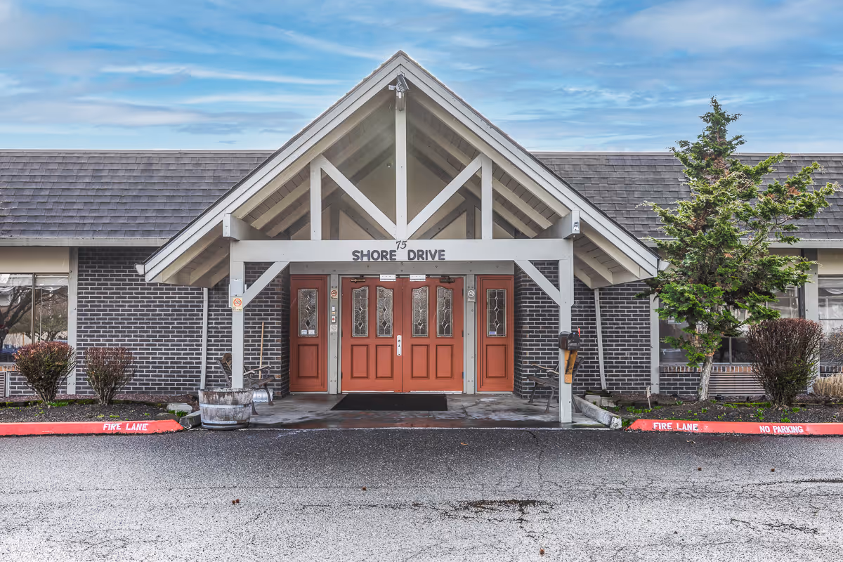 Front entrance of a brick building with a peaked white portico and three red doors beneath a 'Shore Drive' sign.