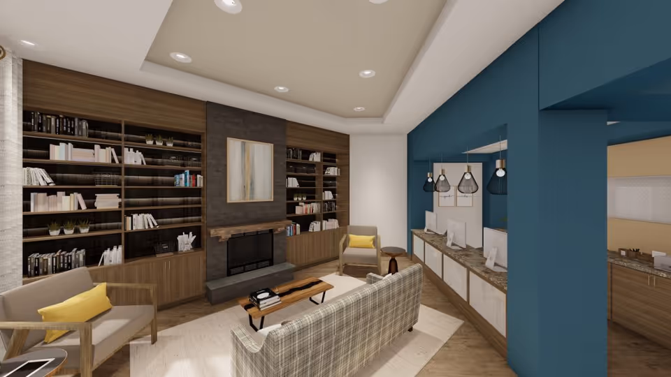 Communal lounge with bookshelves and fireplace, seating area, and a computer workspace under pendant lights.